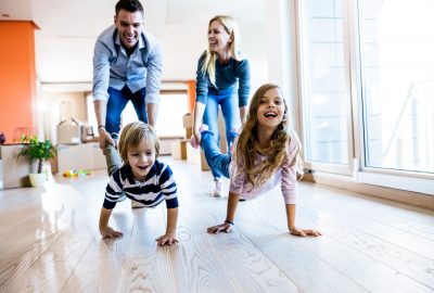 Young happy family having fun while playing wheelbarrow race at their new apartment.